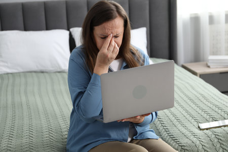 Woman with vision problem using laptop on bed at homeの写真素材