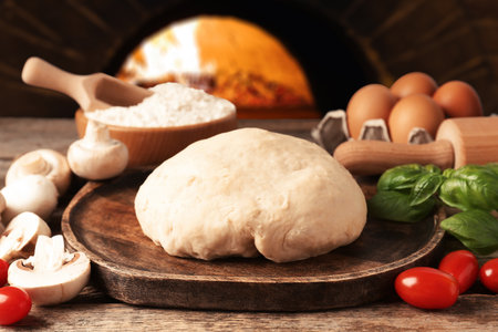 Fresh ingredients for pizza on wooden table against ovenの写真素材