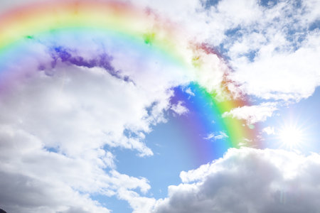 Bright rainbow in blue sky with clouds on sunny day