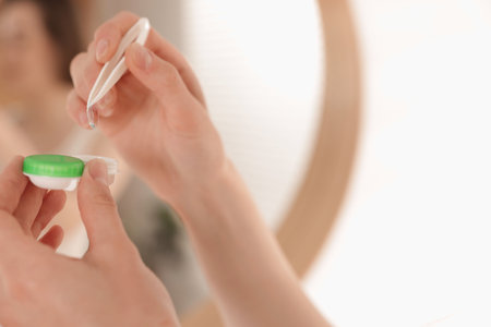 Woman taking contact lens out of case indoors, closeup. Space for textの写真素材