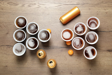 Beer pong game. Plastic cups with drinks, cans and balls on wooden table, flat layの写真素材