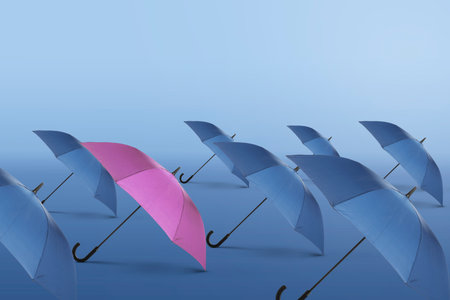 Pink umbrella among blue ones against color gradient backgroundの写真素材