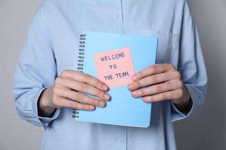 Welcome To The Team. Woman holding notepad with sticky note on grey background, closeupの写真素材