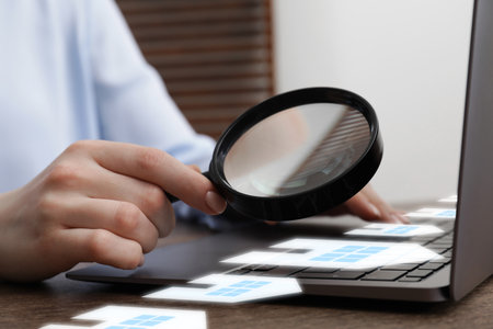 Real estate agent looking at buildings icons with magnifying glass over laptop, closeup. Search for housingの写真素材