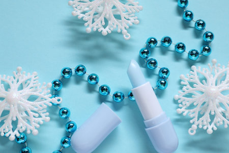 Moisturizing lip balm and Christmas decor on light blue background, flat lay. Winter careの写真素材