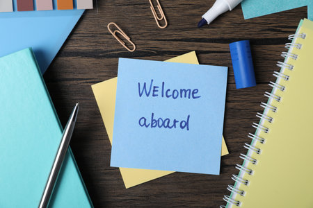 Paper note with phrase Welcome Aboard and stationery on wooden table, flat layの写真素材
