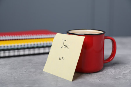Sticky note with phrase Join Us, coffee and notebooks on grey table, closeupの写真素材