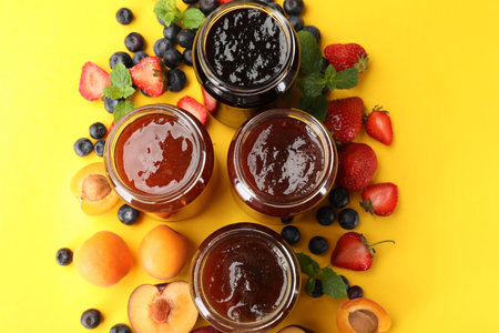 Different jams in jars and ingredients on yellow background, flat lay