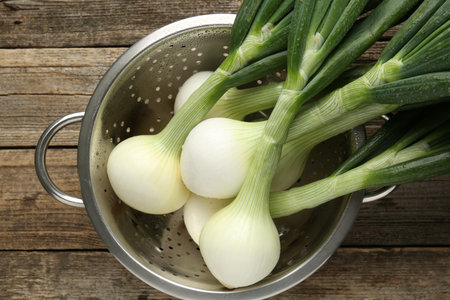 Fresh ripe green onions in colander on wooden table, top viewの写真素材