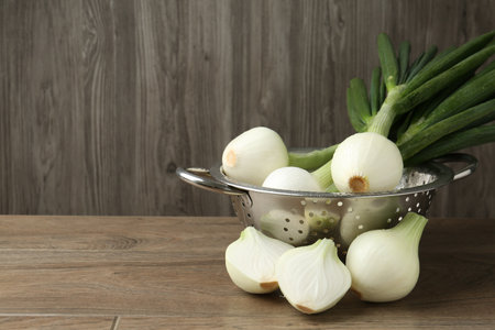 Fresh ripe green onions in colander on wooden table, closeup. Space for textの写真素材