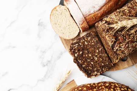 Freshly baked loaves of bread and spikes on white marble table, flat lay. Space for textの写真素材