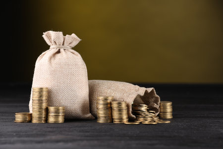 Bags and stacked coins on black table against dark yellow backgroundの写真素材