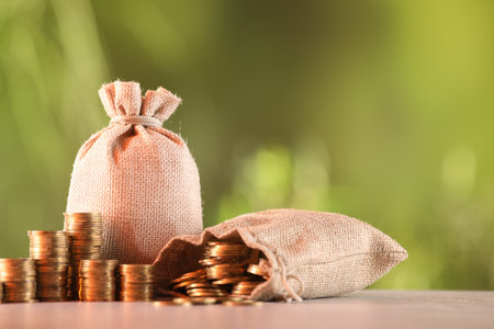 Burlap bags and stacked coins on table against blurred backgroundの写真素材