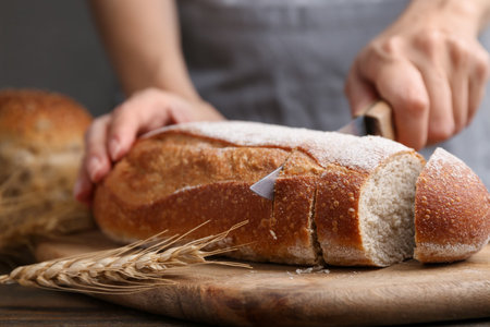 Woman cutting freshly baked bread at wooden table against grey background, closeupの写真素材