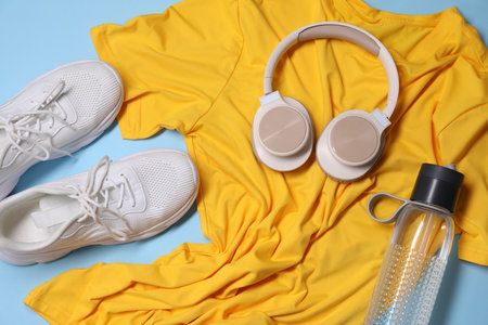Sportswear, bottle of water, headphones and sneakers on light blue background, flat layの写真素材