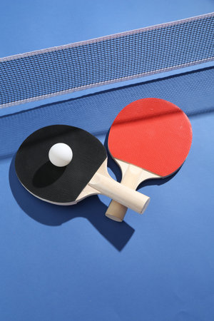 Ping pong rackets, ball and net on blue background