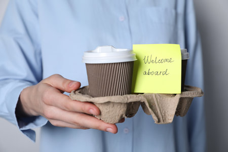 Welcome Aboard. Woman holding holder with takeaway cups and sticky note on grey background, closeupの写真素材