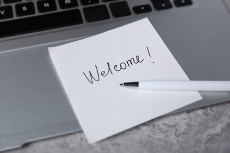 Sticky note with word Welcome, pen and laptop on grey table, closeupの写真素材