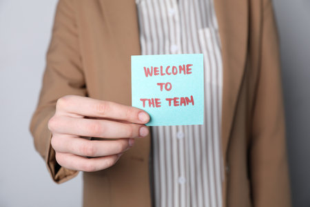 Human resources manager holding sticky note with word Welcome To The Team on grey background, closeupの写真素材