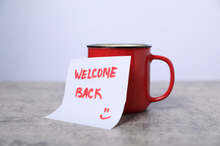 Sticky note with phrase Welcome Back and coffee on grey table, closeupの写真素材
