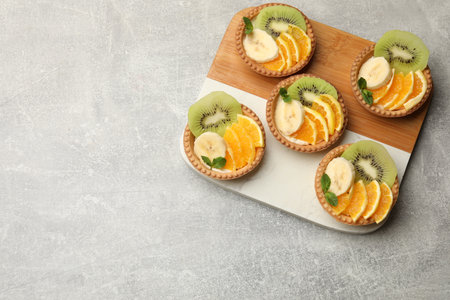 Delicious dessert. Tartlets with fruits and mint on gray textured table, top view. Space for textの写真素材