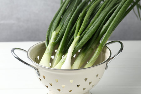 Fresh ripe green onions in colander on white table, closeup