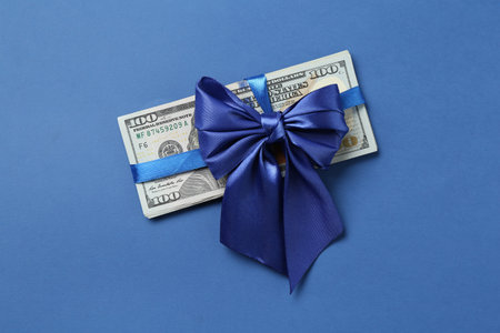 Money bonus. Dollar banknotes with bow on blue background, top view