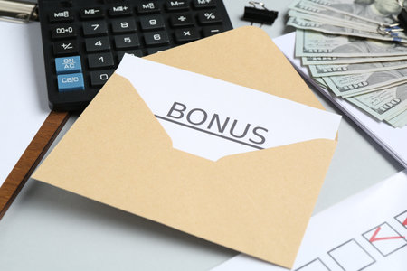 Envelope with word Bonus, money, calculator and paperwork on light grey background, closeupの写真素材