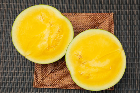 Halves of ripe yellow watermelon on wicker table, top view