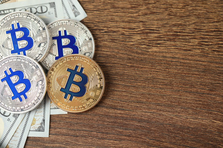 Cryptocurrency. Bitcoins and dollars on wooden table, flat lay. Space for text