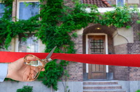 Man cutting red ribbon at opening ceremony of housing estate, closeup