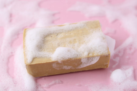 Soap bar with foam on pink background, closeup