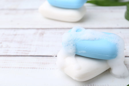 Soap bars with foam on white wooden table, closeup. Space for text