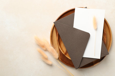 Blank invitation card, envelope, wooden tray and dry spikes on beige background, flat lay. Space for textの写真素材