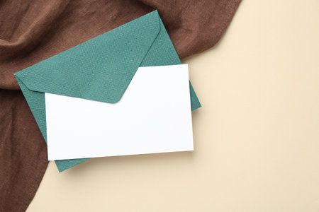 Blank invitation card and envelope on beige background, top view. Space for textの写真素材