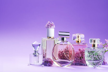 Bottles with perfumes and lilac flowers on purple gradient background, closeup. Space for text