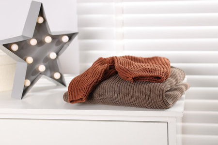 Wool sweaters and star shaped lamp on white nightstand indoorsの写真素材