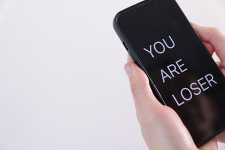 Cyber bullying. Woman holding smartphone with text You Are Loser on white background, closeup. Space for textの写真素材