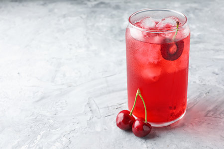 Tasty cherry soda with ice cubes and berries on gray textured table, closeup. Space for textの写真素材