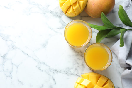 Tasty mango juice in glasses, fresh fruits and leaves on white marble table, flat lay. Space for textの写真素材