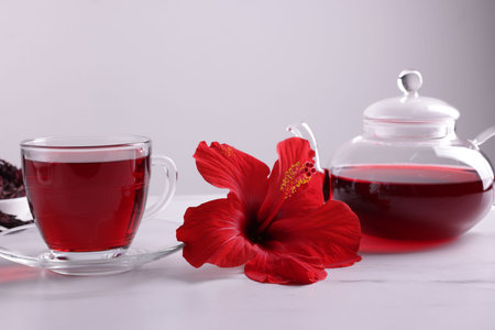 Tasty hibiscus tea and beautiful flower on white table against gray backgroundの写真素材