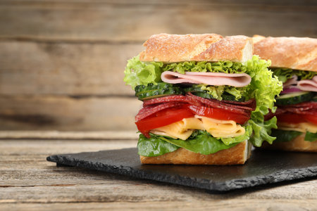 Tasty baguette sandwich with ham and vegetables on wooden table, closeup. Space for textの写真素材