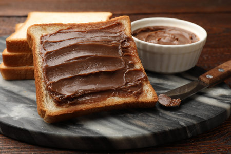Sandwiches with chocolate butter and knife on wooden table, closeup