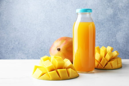 Tasty mango juice in glass bottle and fresh fruits on white marble tableの写真素材