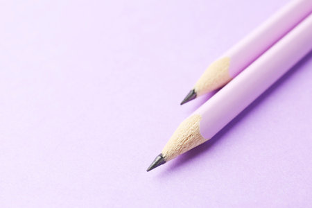Two graphite pencils on violet background, closeup. Space for text