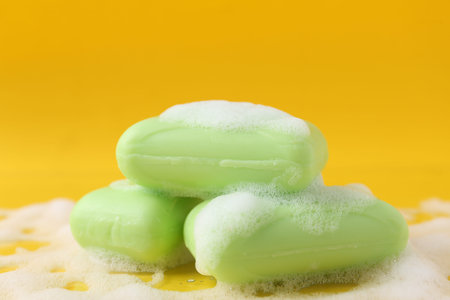Soap bars with foam on yellow background, closeup