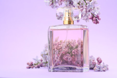Bottle with perfume and lilac flowers on violet gradient background, closeup. Space for textの写真素材