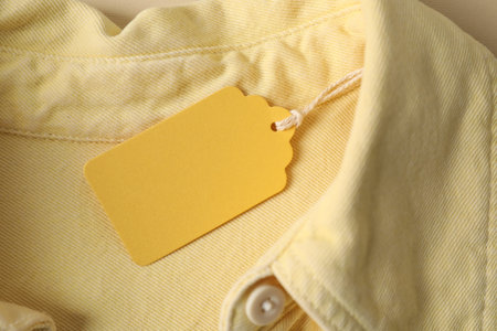 Cardboard tag on pale yellow shirt, top viewの写真素材