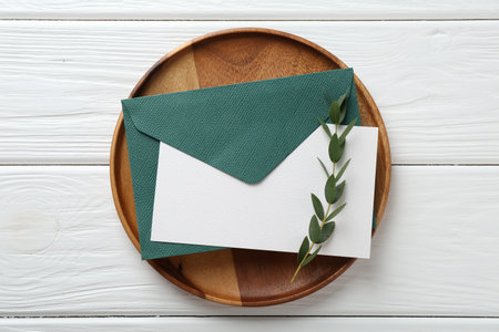 Blank invitation card, envelope, tray and branch on white wooden table, top viewの写真素材