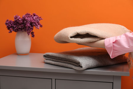 Woman with folded woolen blankets near orange wall indoors, closeupのeditorial素材